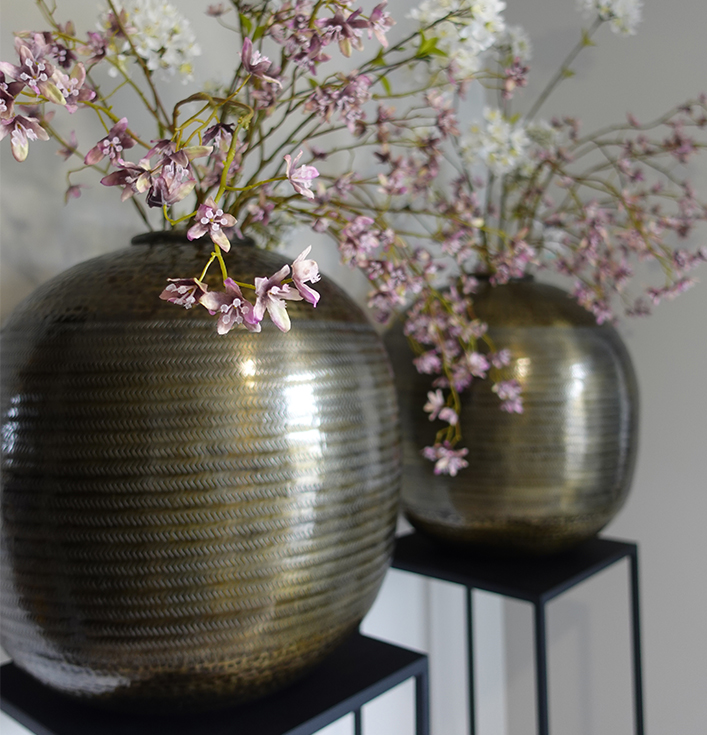 Bolvormige antiek bronzen vazen met paarse kunstbloemen op zwarte zuilen