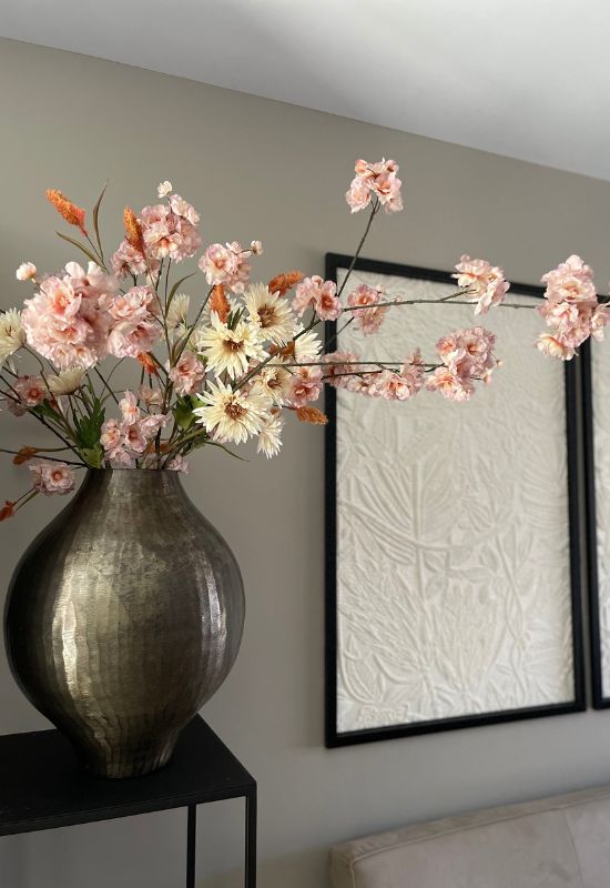 Bronzen vaas op zwarte zuil met roze kunstbloemen