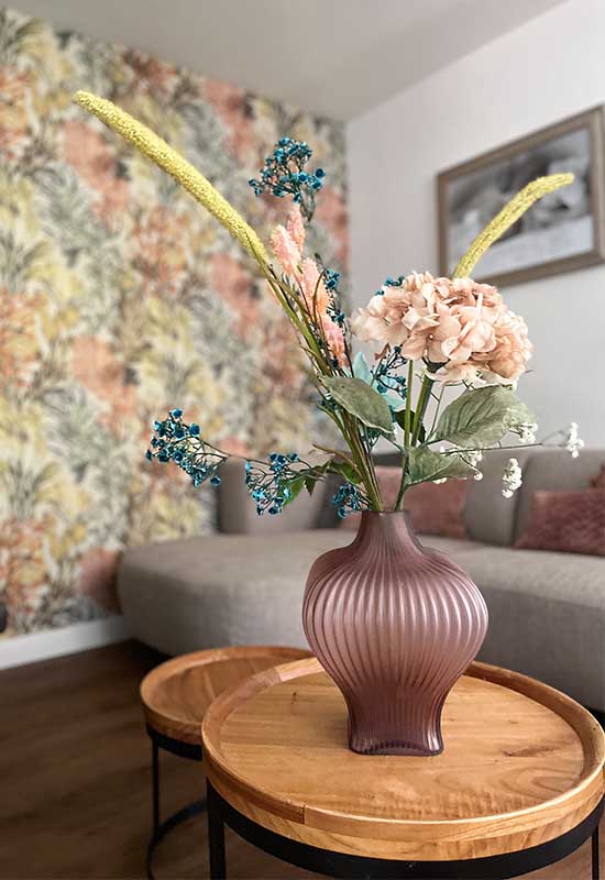 Bruine geribbelde vaas mat glas met kunstbloemen op houten ronde salontafel