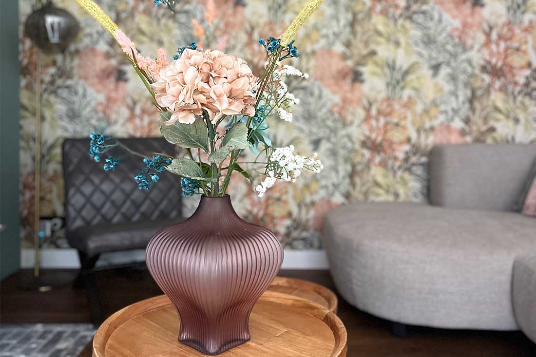 Bruine ribbelvaas mat glas met kunstbloemen op houten ronde salontafel