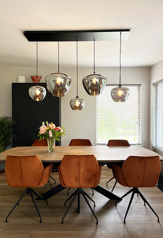 Glazen hanglamp boven houten visgraat eettafel met vijf lichtbronnen roestbruine eetkamerstoelen