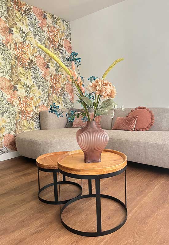 Pastel kleurig interieur koraal print behang beige hoekbank roze sierkussens houten salontafelset