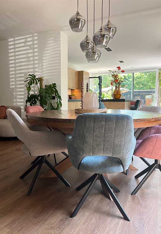 Ronde houten eettafel met grijze, roze en beige eetkamerstoelen glazen hanglamp met rookglas