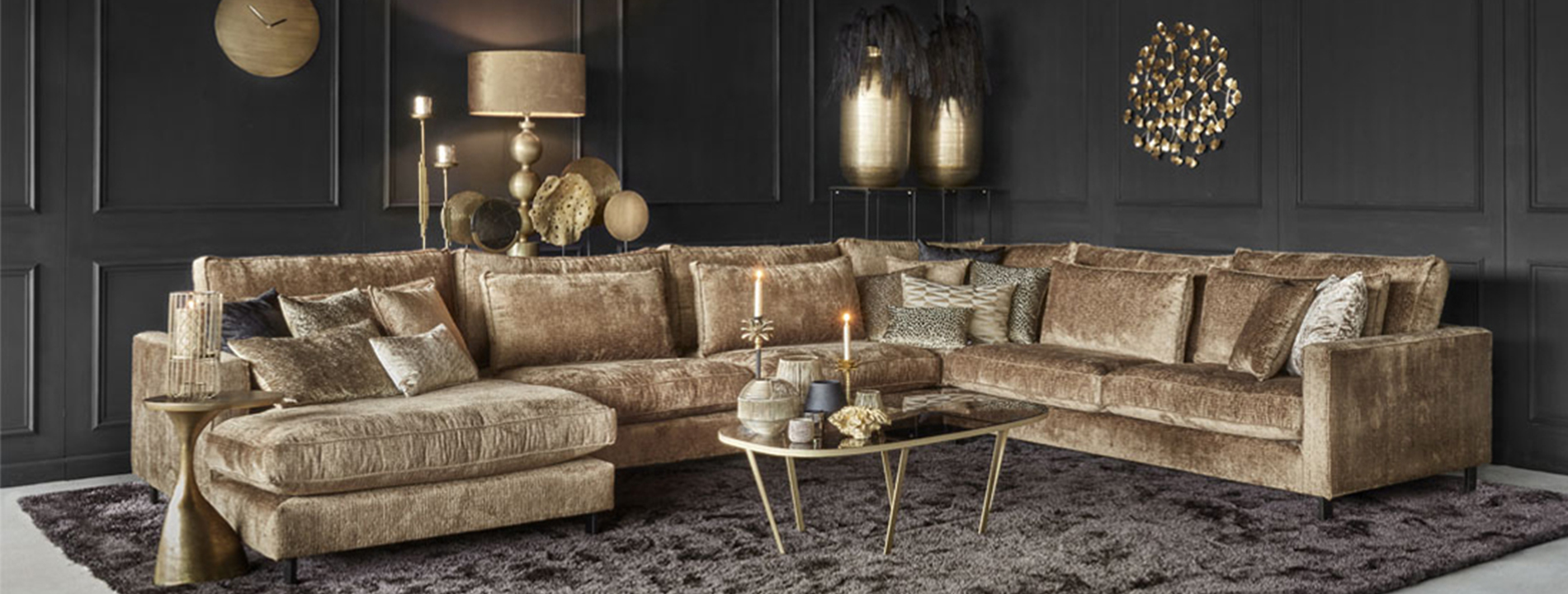 Gouden hoekbank bruin hoogpolig vloerkleed gouden accessoires zwarte muur