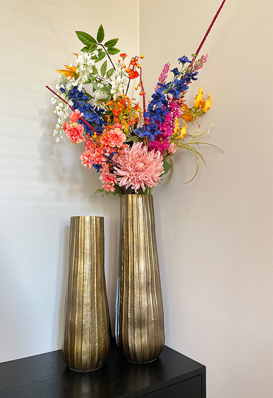 Hoge gouden vazen met ribbels en fleurige kunstbloemen