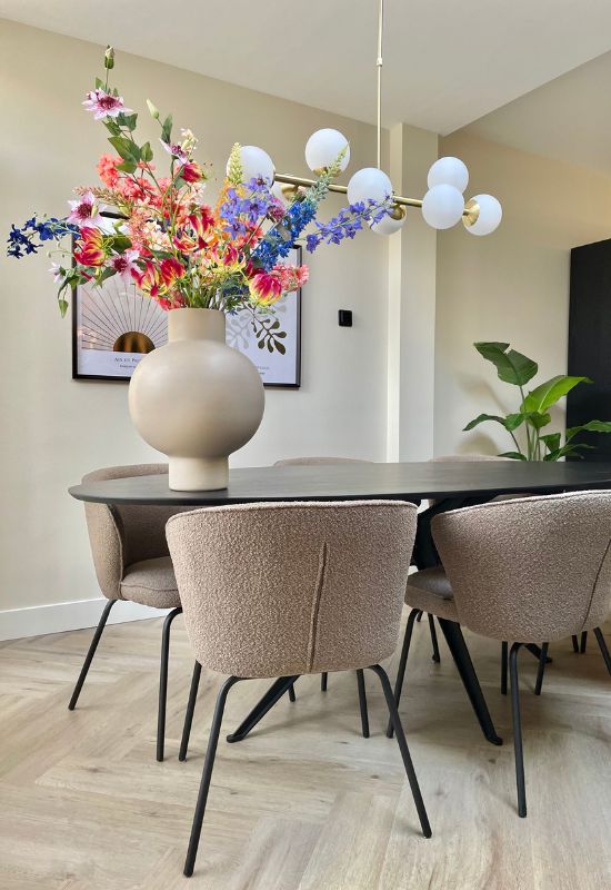 Zwart ovale eettafel beige bouclé eetkamerstoelen beige ronde vaas met fleurig boeket kunstbloemen