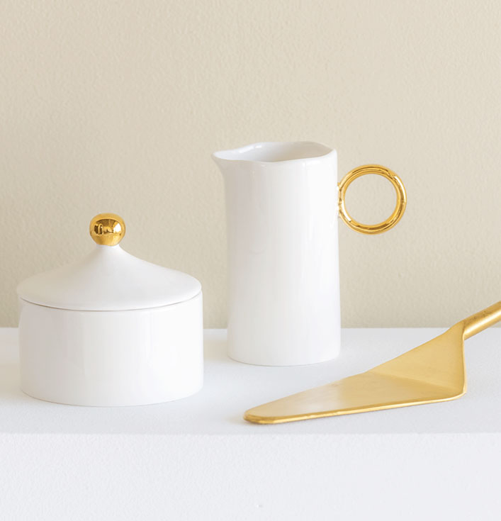 witte suikerpot met witte melkkan en een gouden taartschepper met gouden details
